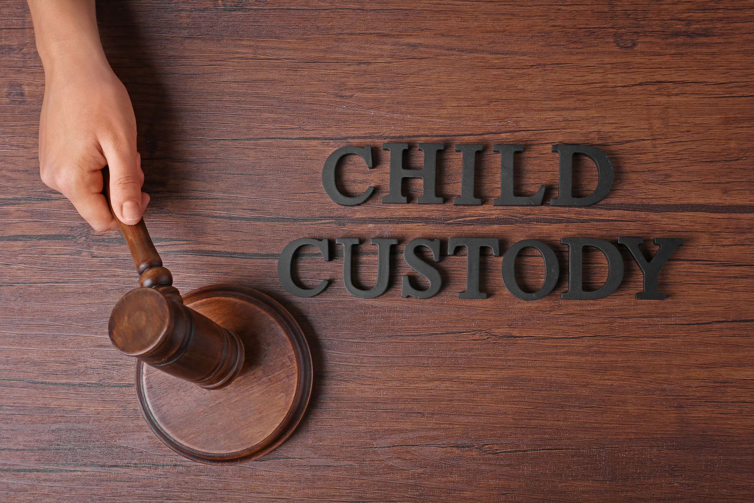 Hand holding court gavel and words CHILD CUSTODY on wooden background, top view